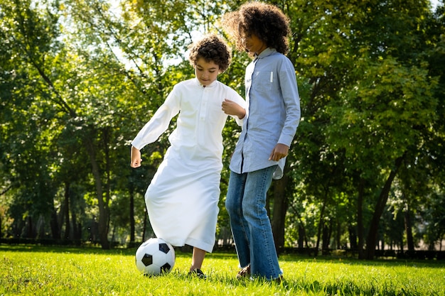 Filmowy obraz rodziny z emiratów spędzającej czas w parku. Brat i siostra grają w piłkę nożną na trawie