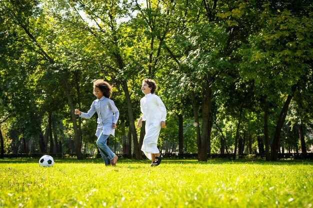 Filmowy obraz rodziny z emiratów spędzającej czas w parku. Brat i siostra grają w piłkę nożną na trawie