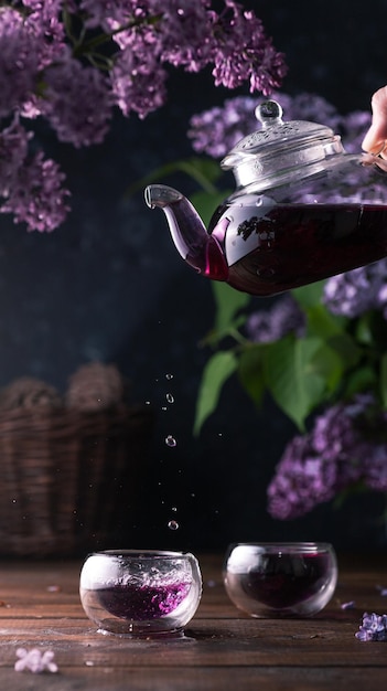Fioletowa herbata nalewa się ze szklanego czajniczka do filiżanek Wokół liliowe kwiaty
