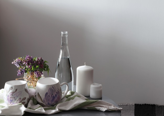 Fioletowe kwiaty, dwie filiżanki, świece, miska z wodą na stole