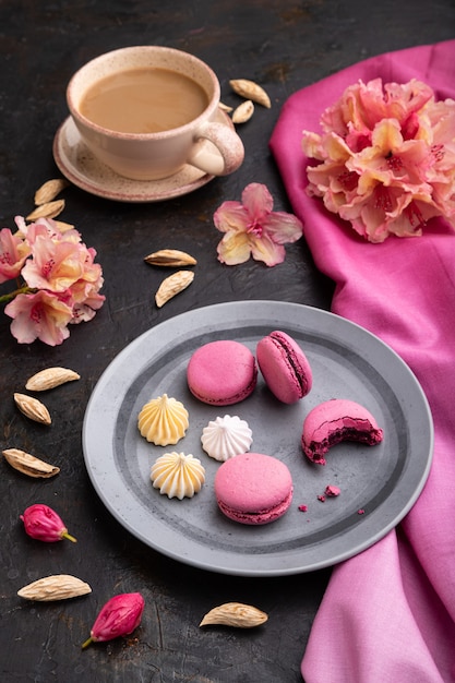 Fioletowe macarons lub macaroons z filiżanką kawy na czarnej betonowej powierzchni i różowej tkaninie
