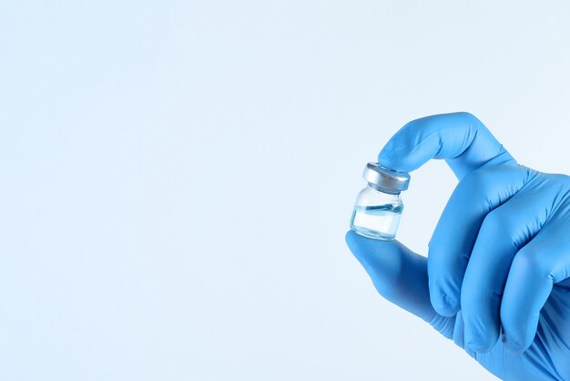Fiolka szczepionki do wstrzykiwań w dłoni lekarza na jasnoniebieskim tle