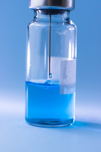 Fiolka z niebieską szczepionką z igłą strzykawki w środku