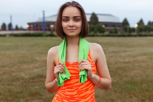 fit biegaczka z ręcznikiem na szyi i w pomarańczowym topie stojąca w polu