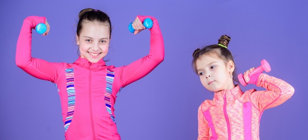 Fit cuties Małe dziewczynki cieszą się treningiem fitness z ciężarkami Śliczne siostry robiące ćwiczenia fitness z hantlami Małe dzieci rozwijające sprawność fizyczną Sport i fitness dla dzieci