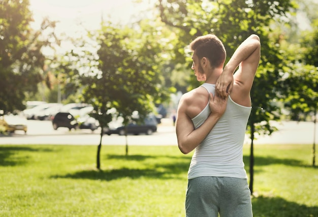 Fitness, człowiek szkolenia jogi w pozie głowa krowy na zewnątrz. Sportowy facet co plecy i ramiona rozciągające się w parku, widok z tyłu, kopia przestrzeń