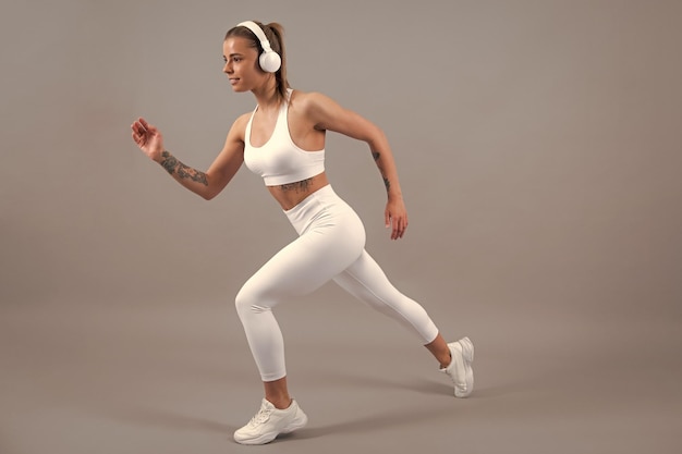 Fitness kobieta biegacz Sportowa silna wesoła młoda kobieta pozuje na szarym tle na białym tle Kaukaski lekkoatletka muskularna sportive kobieta Koncepcja młodości zdrowego stylu życia