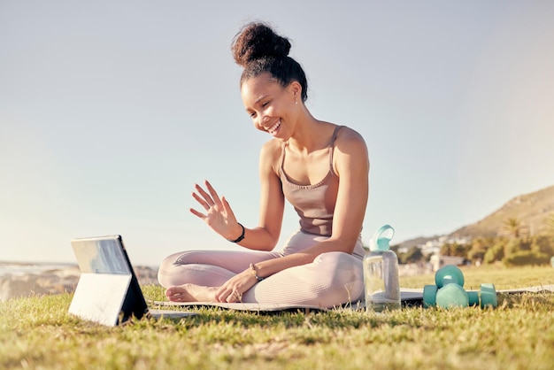 Fitness kobieta i tablet wzywają do treningu jogi lub treningu na trawie na świeżym powietrzu Szczęśliwa kobieta macha do rozmowy wideo na ekranie dotykowym w duchowym wellness zen lub stylu życia w przyrodzie