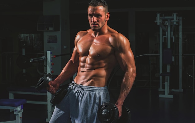 Fitness muskularne ciało Trening na siłowni Mężczyzna kulturysta robi ćwiczenia z hantlami