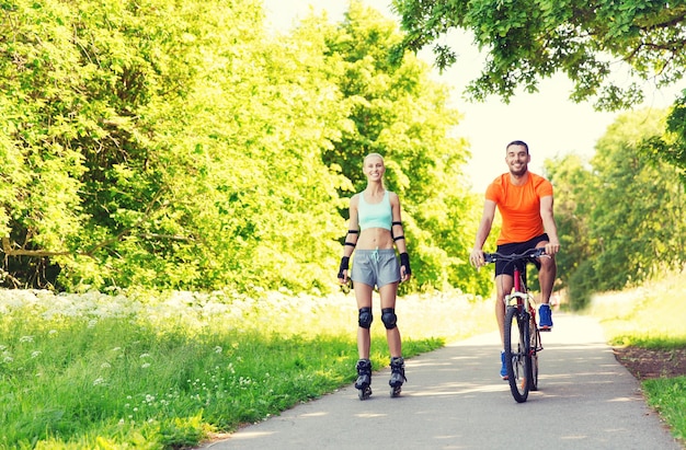 fitness, sport, lato, ludzie i koncepcja zdrowego stylu życia - szczęśliwa para z rolkami i jazdą na rowerze na świeżym powietrzu latem