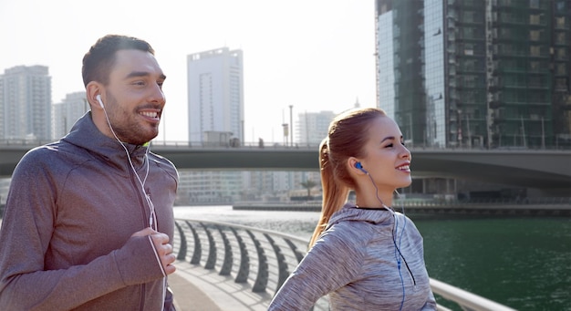 fitness, sport, ludzie, technologia i koncepcja stylu życia - szczęśliwa para biegająca i słuchająca muzyki w słuchawkach na tle ulicy dubaju