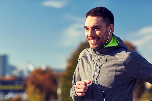 fitness, sport, ludzie, technologia i styl życia koncepcja - szczęśliwy człowiek biegający i słuchający muzyki w słuchawkach w mieście