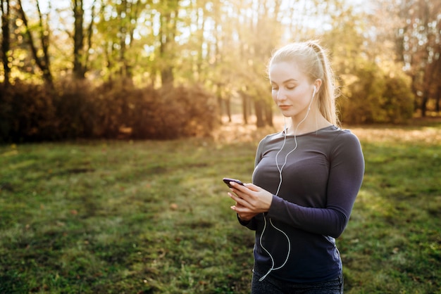 Fitness w parku. Dziewczyna trzyma w ręku smartfon i słuchawki.