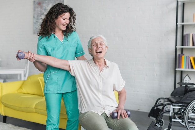 Zdjęcie fizyczny terapeuta pomaga starszej kobiety dla robić ćwiczeniu z dumbbell