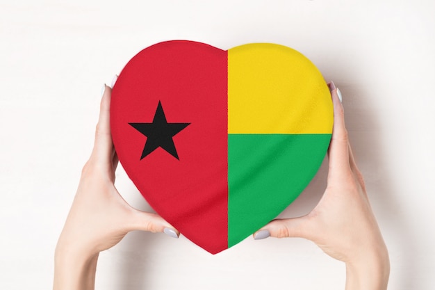 Flaga Gwinei Bissau na pudełku w kształcie serca w rękach kobiet. białe tło