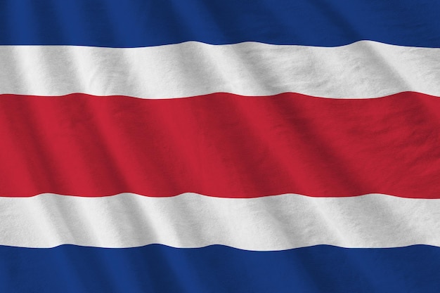 Flaga Kostaryki z dużymi fałdami macha z bliska pod światłem studyjnym w pomieszczeniu Oficjalne symbole i kolory na banerze