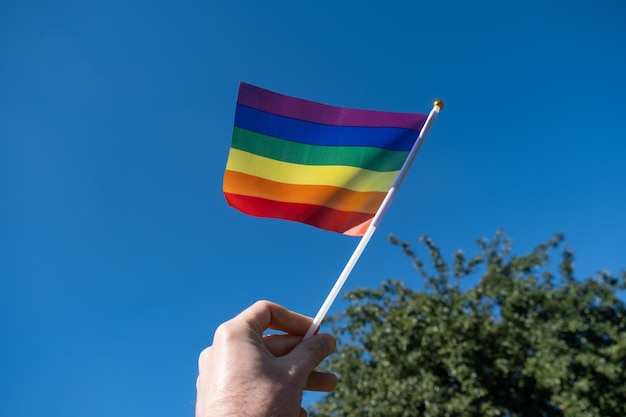 Flaga LGBT w dłoni mężczyzny na tle błękitnego nieba.