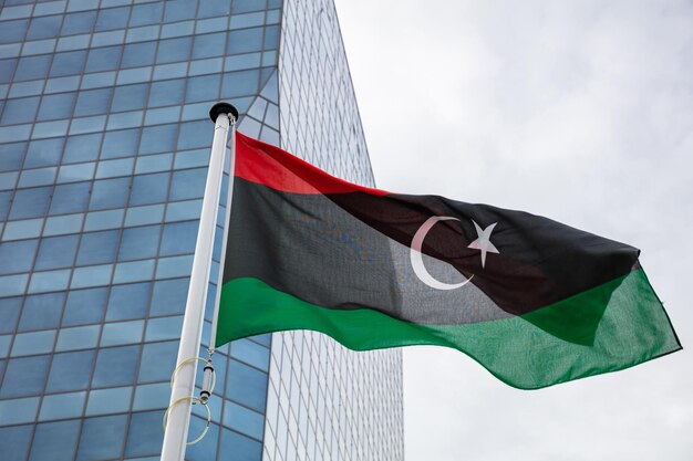Flaga libii na słupie macha nowoczesnym tłem budynku biurowego