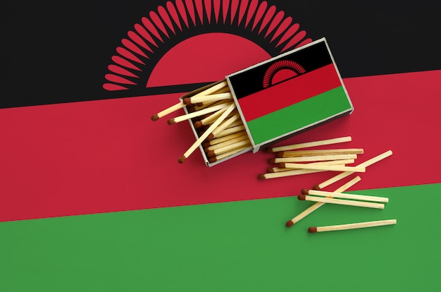 Flaga Malawi jest pokazana na otwartym pudełku zapałek, z którego wypada kilka zapałek i leży na dużej fladze