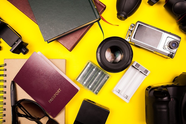 Flatlay widok z góry zestawu podróżnego na żółtym tle w studiop photo. Obok innych akcesoriów paszport, książki, aparat z obiektywem, papier i okulary przeciwsłoneczne