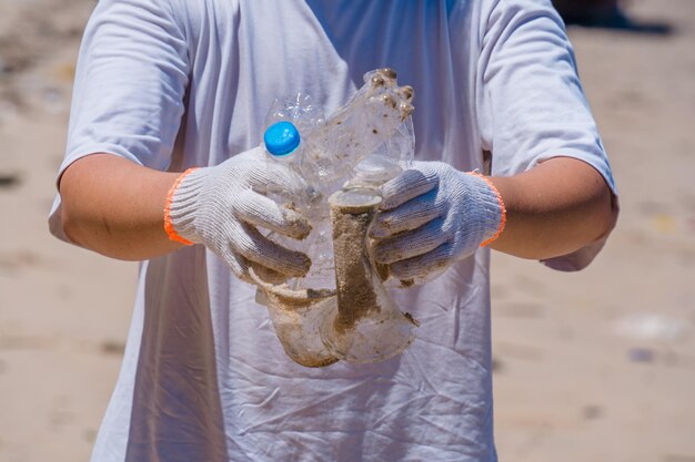 Focus Wolontariusz w rękawiczkach zbierający śmieci z butelek na plaży parkowej Sprzątanie przyrody