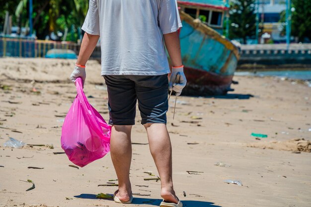 Focus Wolontariusz w rękawiczkach zbierający śmieci z butelek na plaży parkowej Sprzątanie przyrody