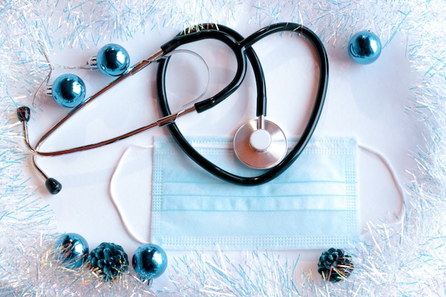Fonendoskop i maska medyczna na jasnym tle z noworocznym blichtrem i zabawkami. Koncepcja opieki zdrowotnej i medycyny.