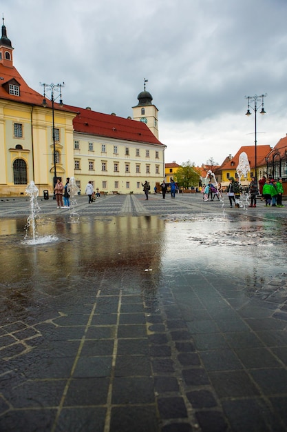 Fontanna na środku placu otoczona jest żółtym budynkiem.