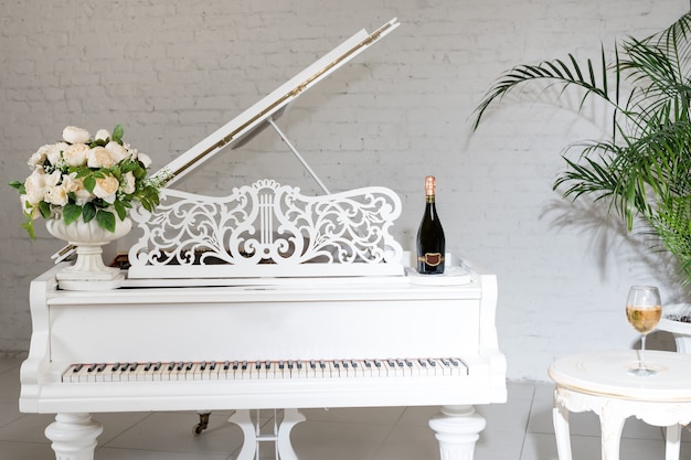 Fortepian w luksusowym białym klasycznym wnętrzu z winem, palmami i kwiatami