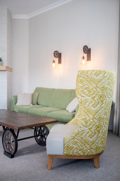 Fotel, salon. Designerski tapicerowany fotel z wysokim oparciem, wzorzystą powierzchnią w pobliżu niskiego stolika i sofy w salonie