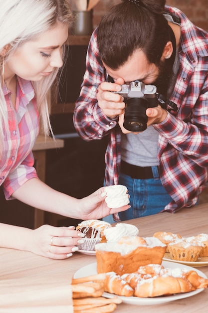 Fotograf kulinarny i asystent w pracy. Mężczyzna i kobieta biorąc zdjęcie bezy. Wokół asortyment ciast i ciastek.