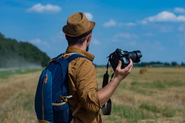 Fotograf podróżnik z aparatem w dłoni na tle pola i stogów siana