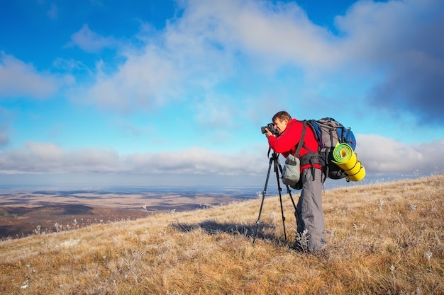 Fotograf robi zdjęcia na szczycie góry jesienią. Podróżnik z plecakiem cieszący się widokiem ze szczytu góry