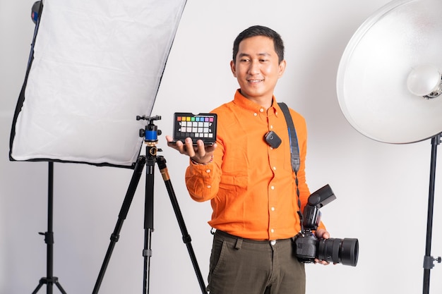 Fotograf trzyma paletę kolorów, niosąc aparat ze sprzętem oświetleniowym na odosobnionym backgro