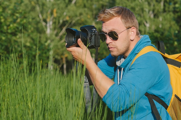 Fotograf trzyma w rękach profesjonalną kamerę foto-video. Na tle zieleni i lasu.