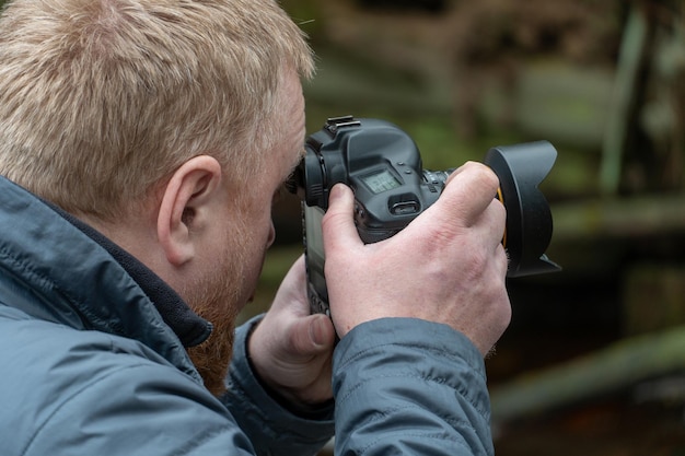 Zdjęcie fotograf w lesie profesjonalny aparat w rękach fotografowanie przyrody i krajobrazu modny młody chłopak z brodą trzyma aparat