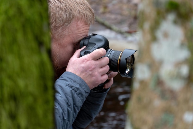 Zdjęcie fotograf w lesie profesjonalny aparat w rękach fotografowanie przyrody i krajobrazu modny młody chłopak z brodą trzyma aparat