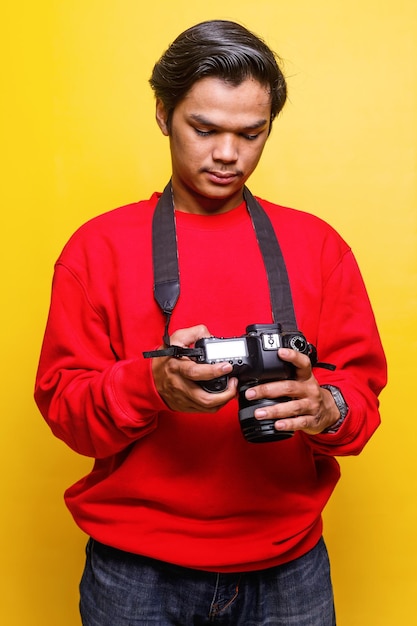 fotograf w swobodnym stylu trzyma aparat i sprawdza wynik zdjęcia na żółtym tle