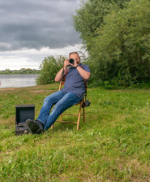 Fotograf z aparatem siedzi latem na brzegu nad rzeką