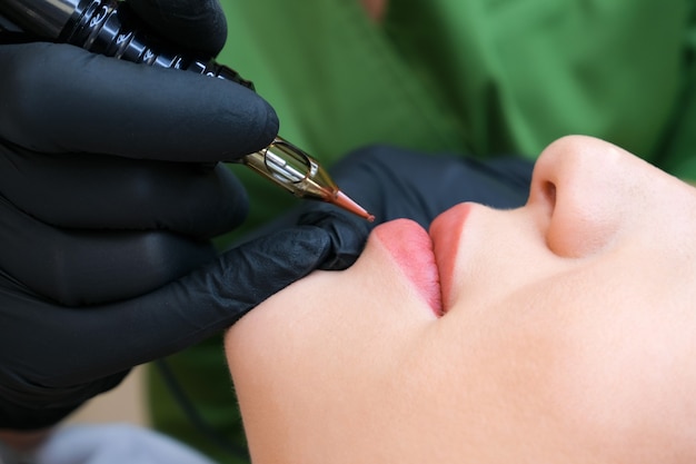 Fotografia makro procesu nakładania makijażu permanentnego w naturalnym kolorze na ustach kobiety.