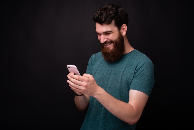 Fotografia młody brodaty mężczyzna używa jego ono uśmiecha się i smartphone