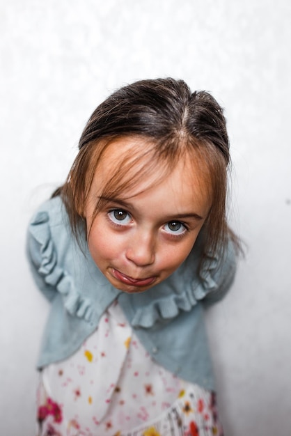 Fotografia portret małej dziewczynki krzywiącej się wygłupiającej się na białym tle na jasnym tle