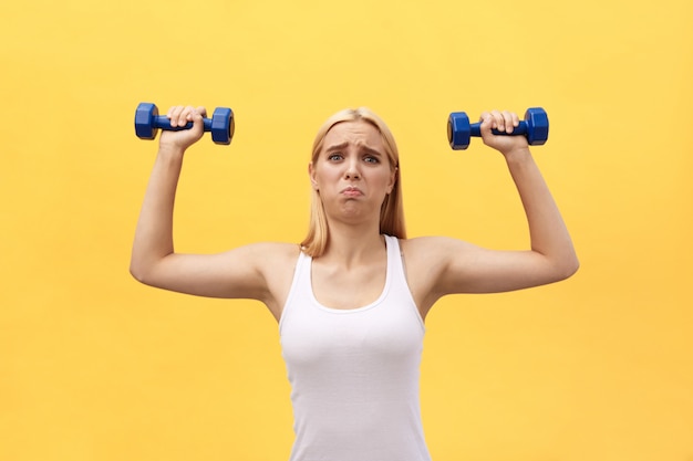 Fotografia poważna młoda sport kobieta robi ćwiczeniom z dumbbells odizolowywającymi nad kolor żółty ściany tłem.