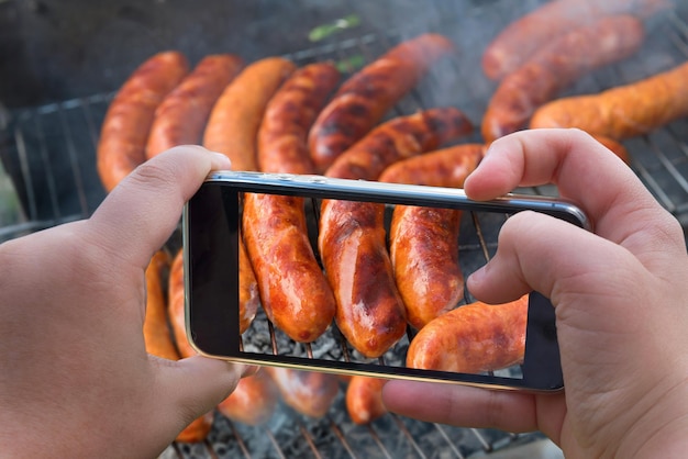 Fotografia żywności pieczonych kiełbasek zdjęcie szaszłyków z pieczonego mięsa z rękami smartfona