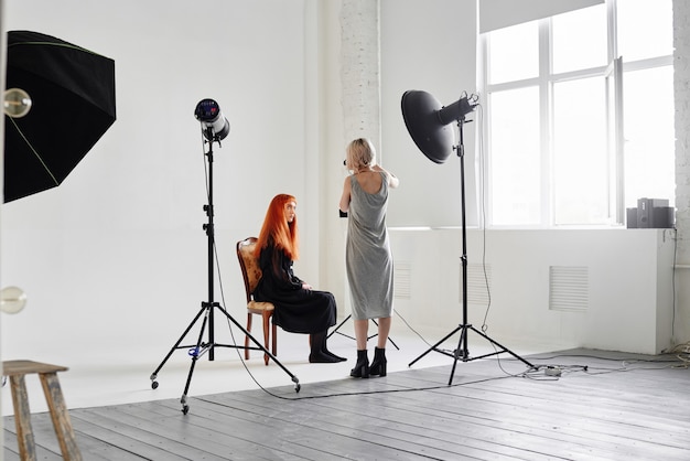 Fotografka fotografująca modelka w czerni, siedząca na krześle na białym tle w Studio