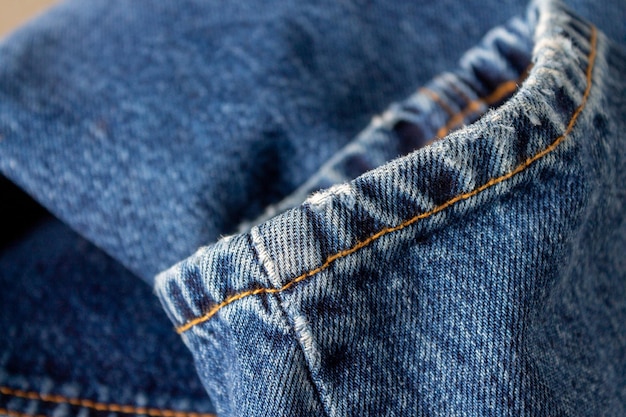 Fragment niebieskich jeansowych spodni przeszytych pomarańczowymi nitkami, selektywne skupienie