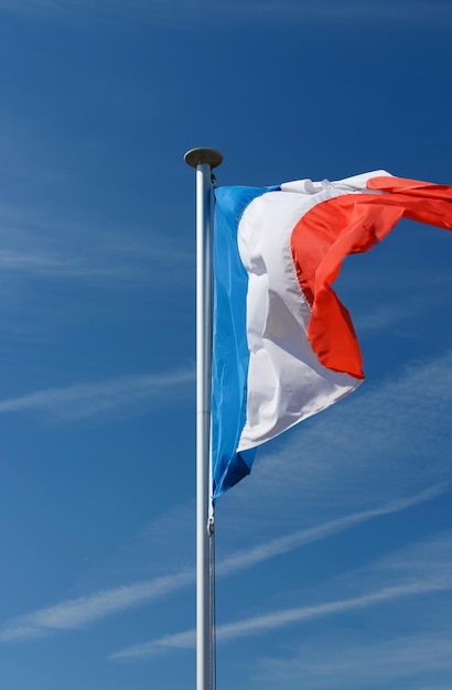 Francuska flaga Tricolor machająca z masztu flagowego na tle błękitnego nieba