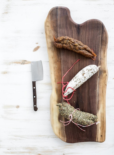 Francuskie salami wędzone z alzackiego na rustykalnej drewnianej desce do krojenia z orzecha włoskiego na białym tle widok z góry