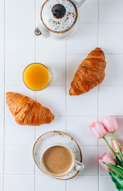 Francuskie śniadanie z rogalikami z sokiem pomarańczowym i kawą z różowymi tulipanami
