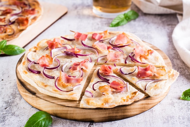 Francuskie tarte flammkuchen z serkiem, cebulą i boczkiem na desce na stole